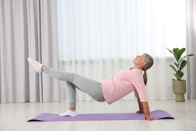 Senior woman practicing yoga on mat at home