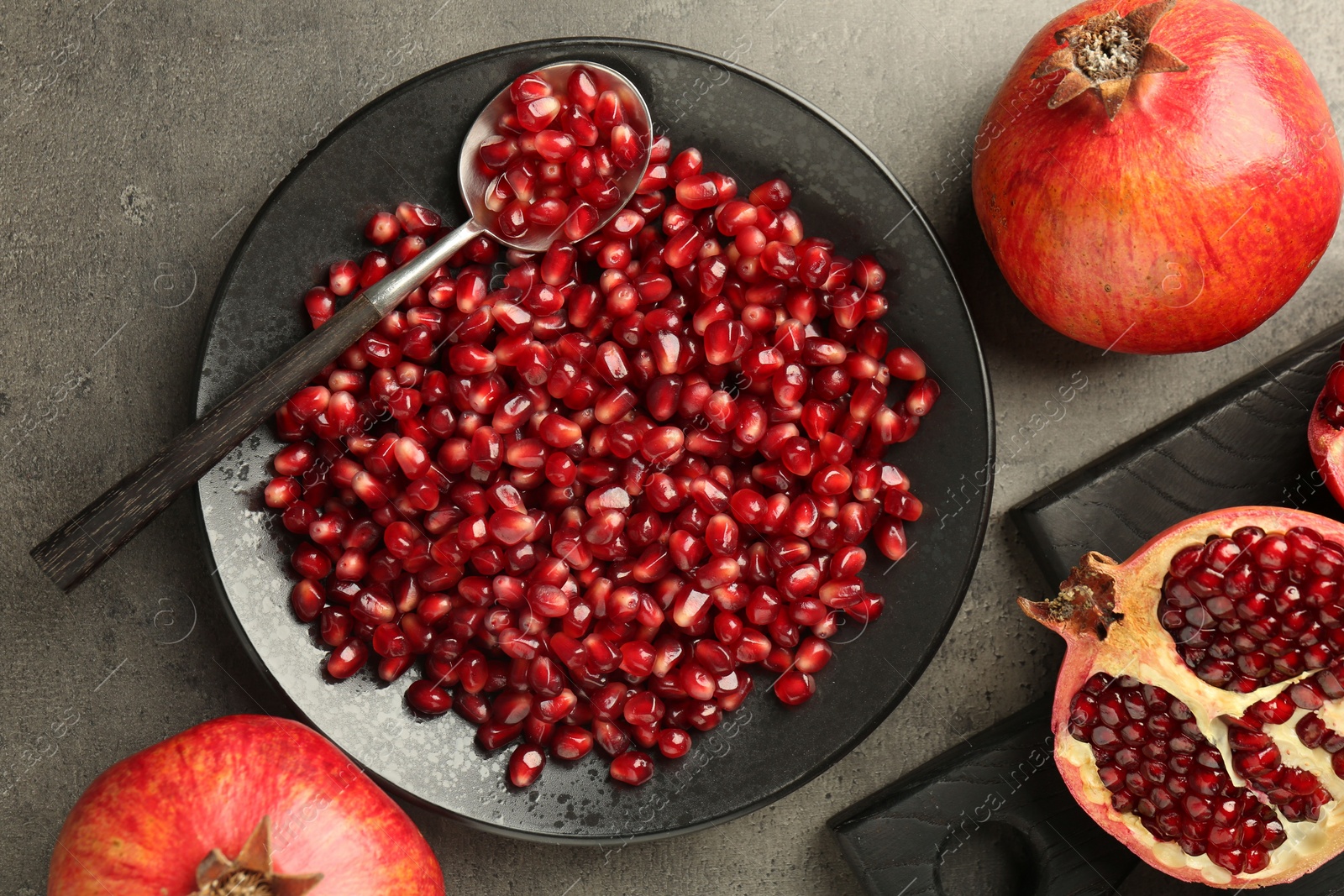 Photo of Ripe juicy pomegranates with grains on grey textured table, flat lay