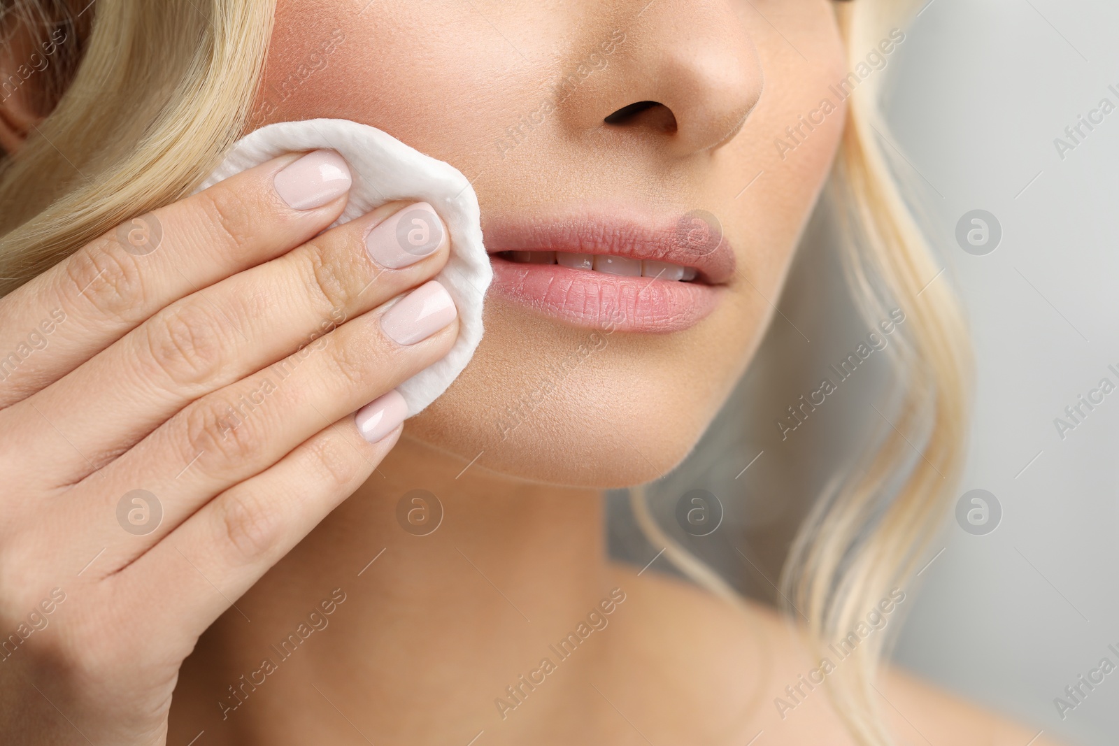 Photo of Woman removing makeup with cotton pad on blurred background, closeup