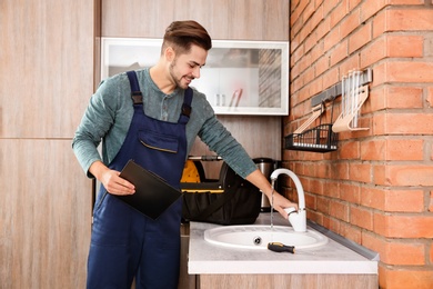 Photo of Male plumber in uniform checking faucet in kitchen. Repair service