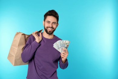 Portrait of happy young man with money and shopping bags on color background. Space for text