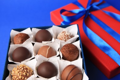 Box with delicious chocolate candies on blue background, closeup