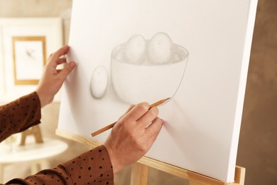 Photo of Woman drawing bowl of fruits with graphite pencil on canvas indoors, closeup