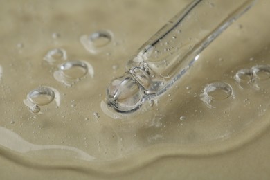 Pipette with cosmetic serum on beige background, closeup