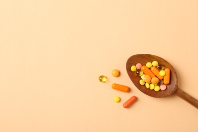 Photo of Wooden spoon with different pills and space for text on color background, top view