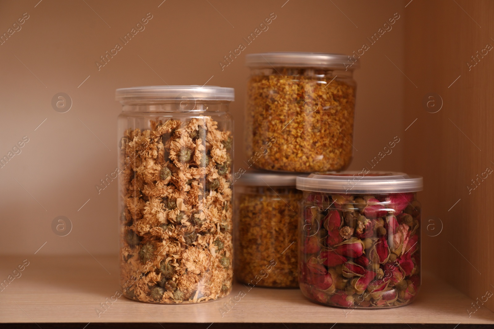 Photo of Glass jars with different dry herbs for tea on wooden shelf