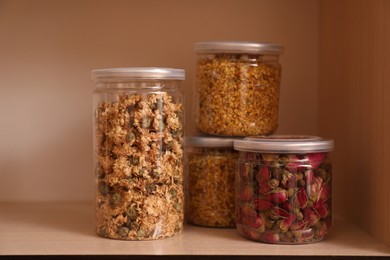 Glass jars with different dry herbs for tea on wooden shelf