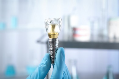 Dentist holding educational model of dental implant on blurred background, closeup