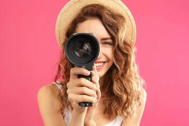 Photo of Beautiful young woman using vintage video camera against crimson background, focus on lens