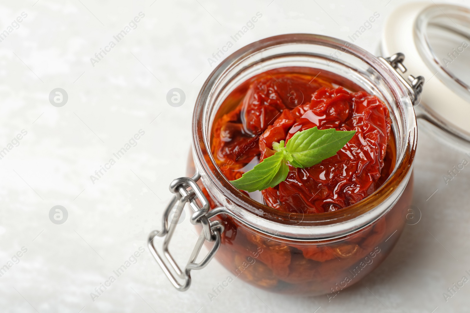 Photo of Jar with sun dried tomatoes on light table. Space for text