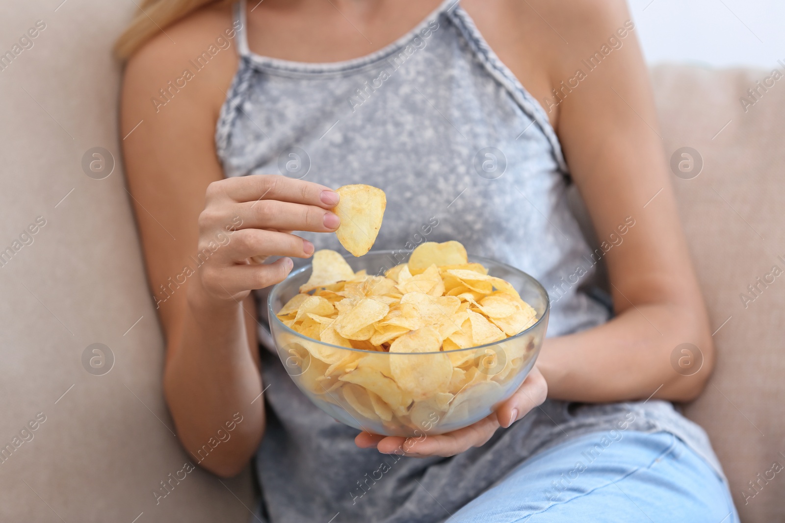 Photo of Woman with bowl of potato chips sitting on sofa, closeup