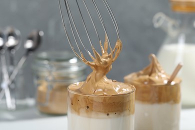 Putting cream for dalgona coffee into glass on table, closeup