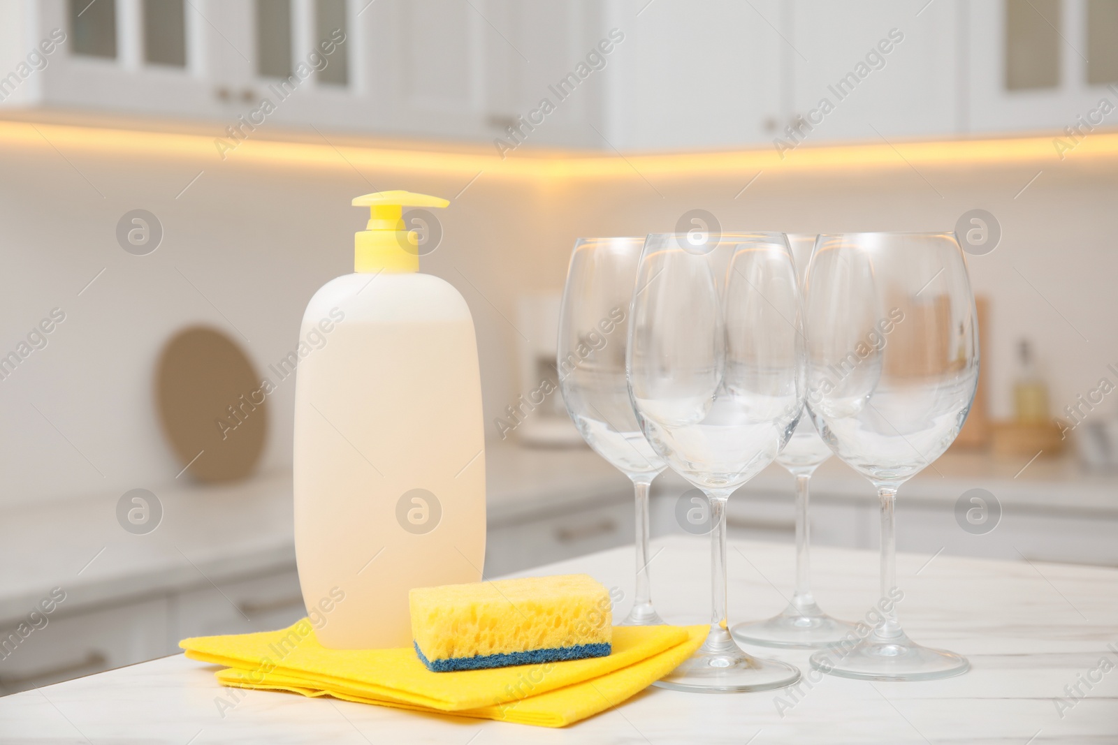 Photo of Clean glasses and cleaning product on table in stylish kitchen