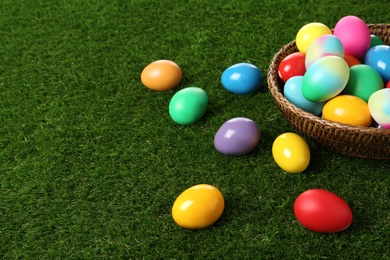 Photo of Wicker basket with bright painted Easter eggs on green grass. Space for text