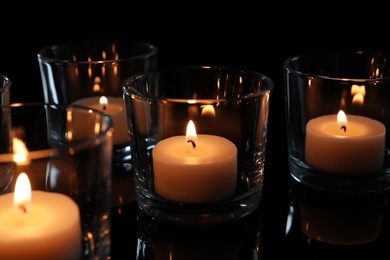 Wax candles burning on table in darkness, closeup