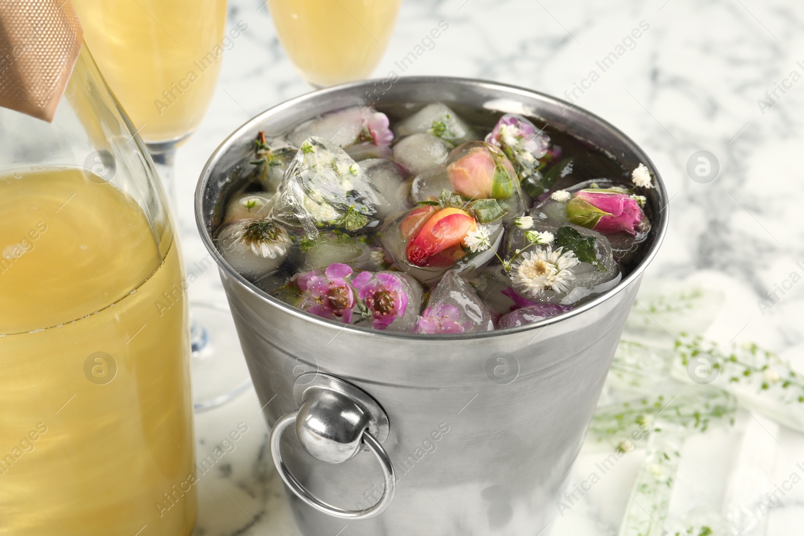 Photo of Bucket of water with floral ice cubes and champagne bottle on table