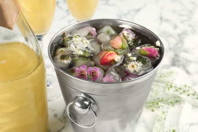 Photo of Bucket of water with floral ice cubes and champagne bottle on table