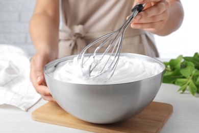 Photo of Woman whipping white cream with balloon whisk at wooden table, closeup