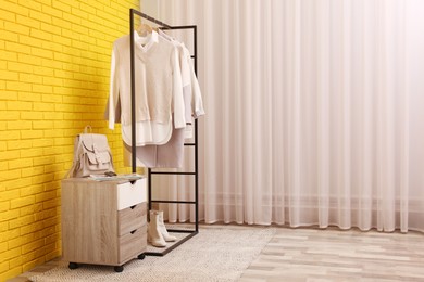 Rack with stylish clothes near yellow brick wall indoors, space for text