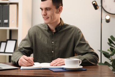 Photo of Man taking notes at wooden table in office, selective focus