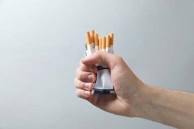 Photo of Stop smoking. Man holding pack with cigarettes on grey background, closeup