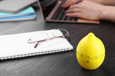 Woman working on laptop at wooden table, focus on kitchen timer in shape of lemon. Space for text