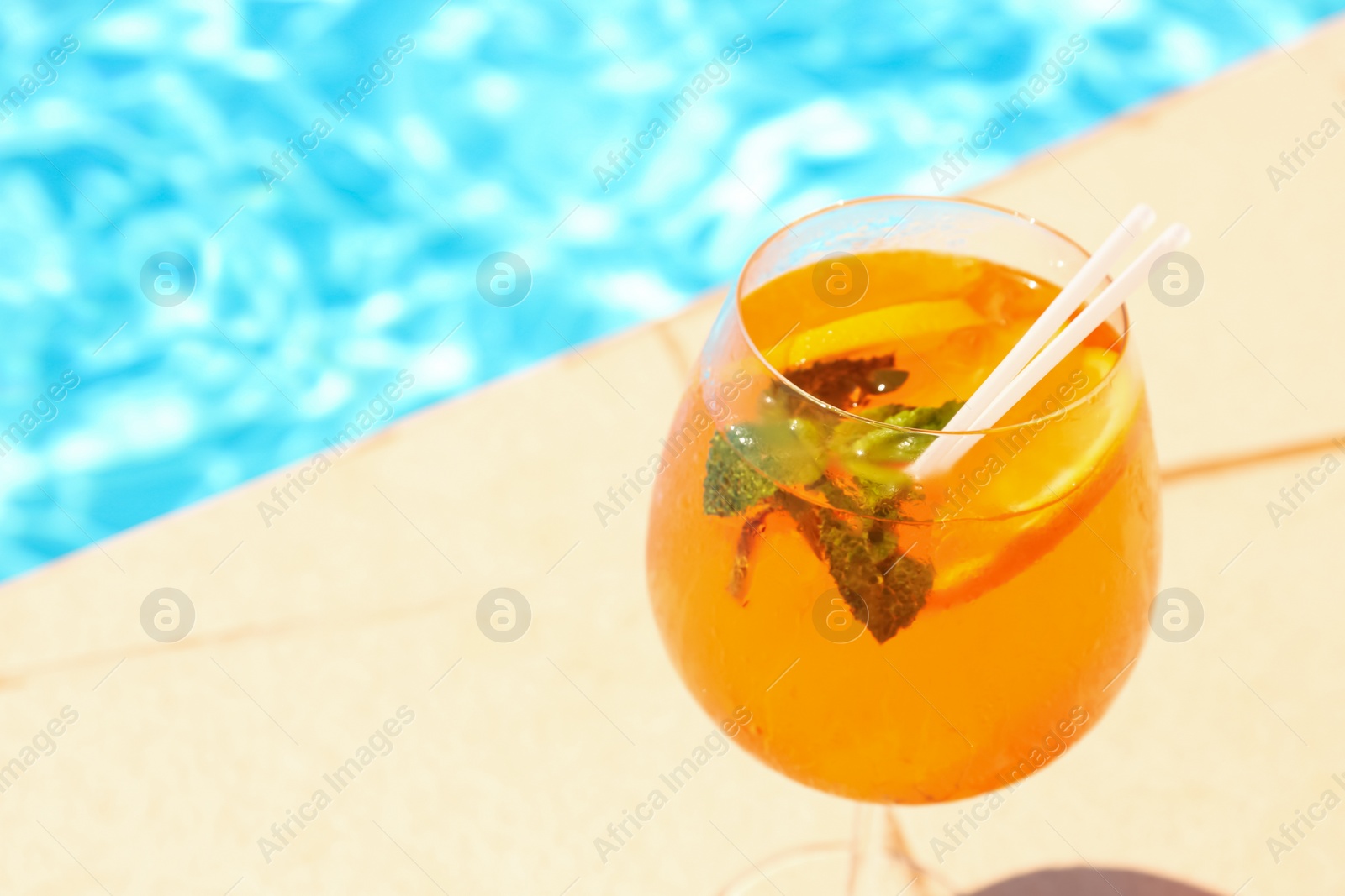 Photo of Glass of delicious cocktail near swimming pool, space for text. Refreshing drink