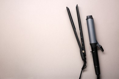 Photo of Curling iron and hair straightener on grey background, flat lay. Space for text