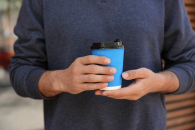 Man with takeaway coffee cup outdoors, closeup