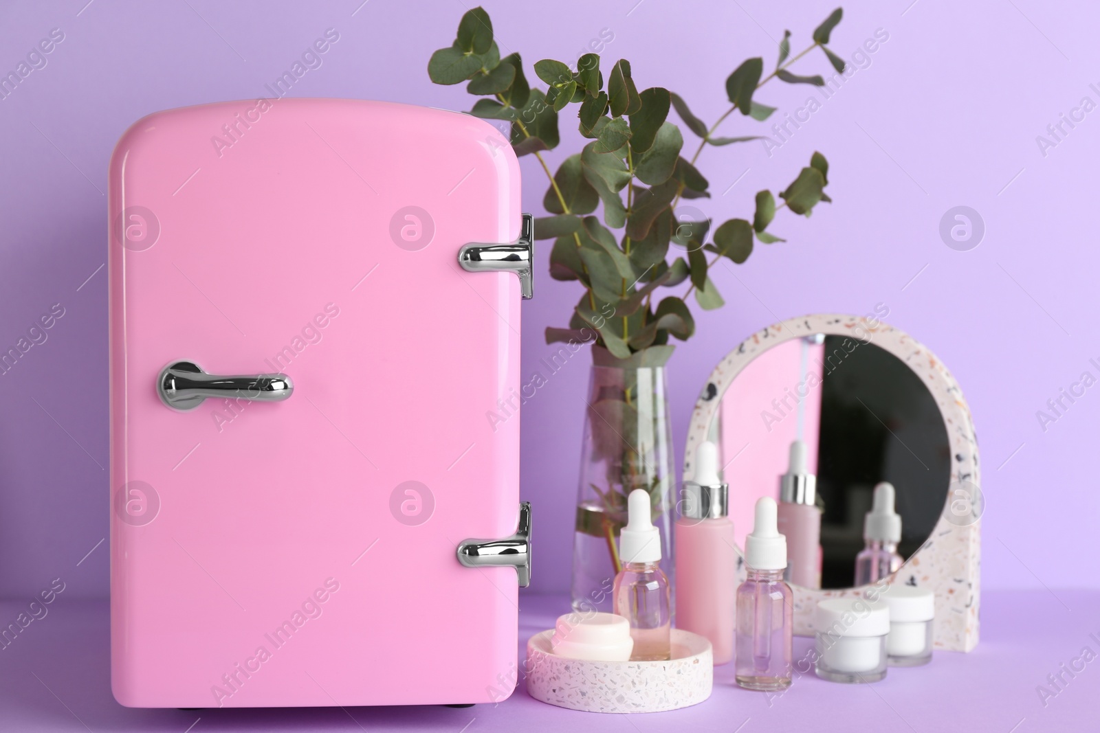 Photo of Cosmetic refrigerator and skin care products on violet background