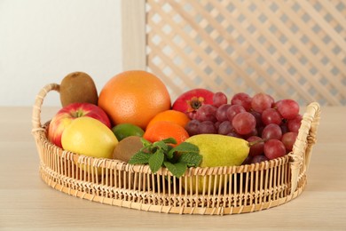Photo of Fresh ripe fruits in wicker tray on wooden table