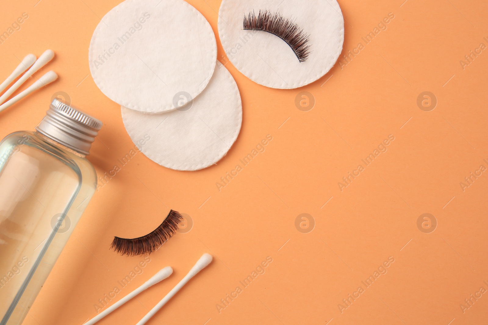 Photo of Flat lay composition with makeup remover and false eyelashes on pale orange background, space for text