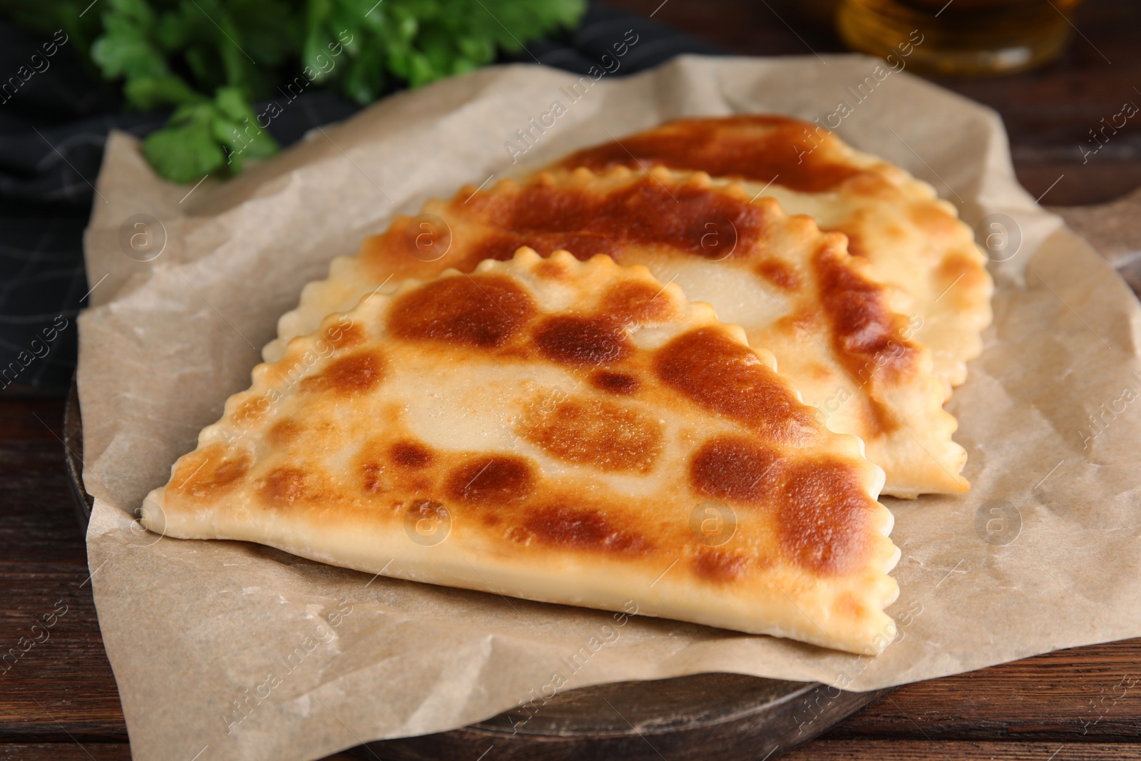 Photo of Board with delicious fried chebureki on wooden table, closeup