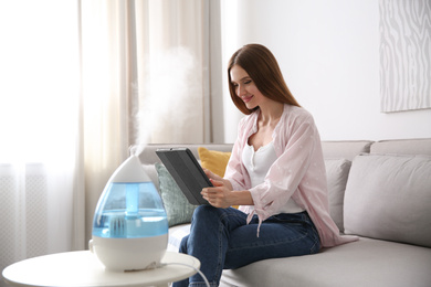 Photo of Woman using tablet in room with modern air humidifier