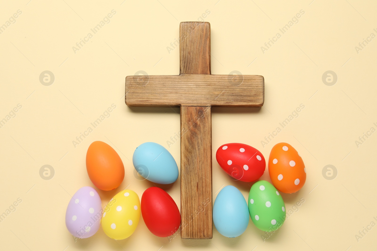 Photo of Wooden cross and painted Easter eggs on beige background, flat lay