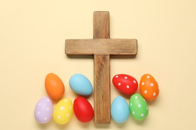 Wooden cross and painted Easter eggs on beige background, flat lay