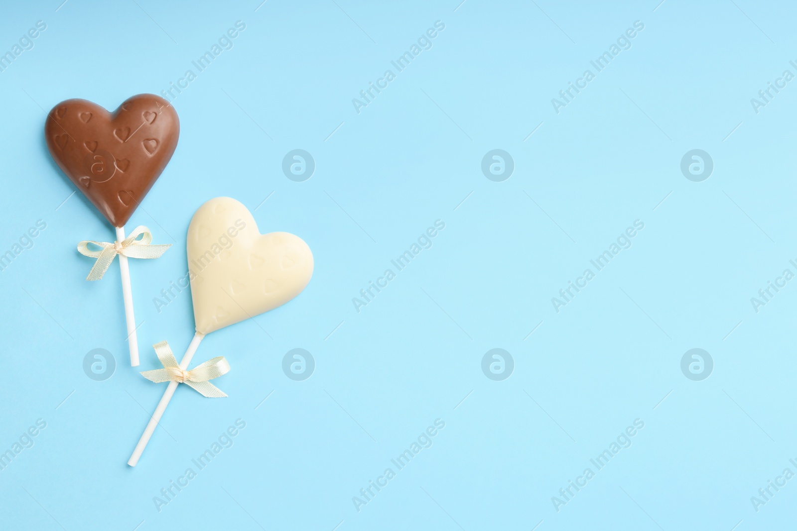 Photo of Different chocolate heart shaped lollipops on turquoise background, flat lay. Space for text