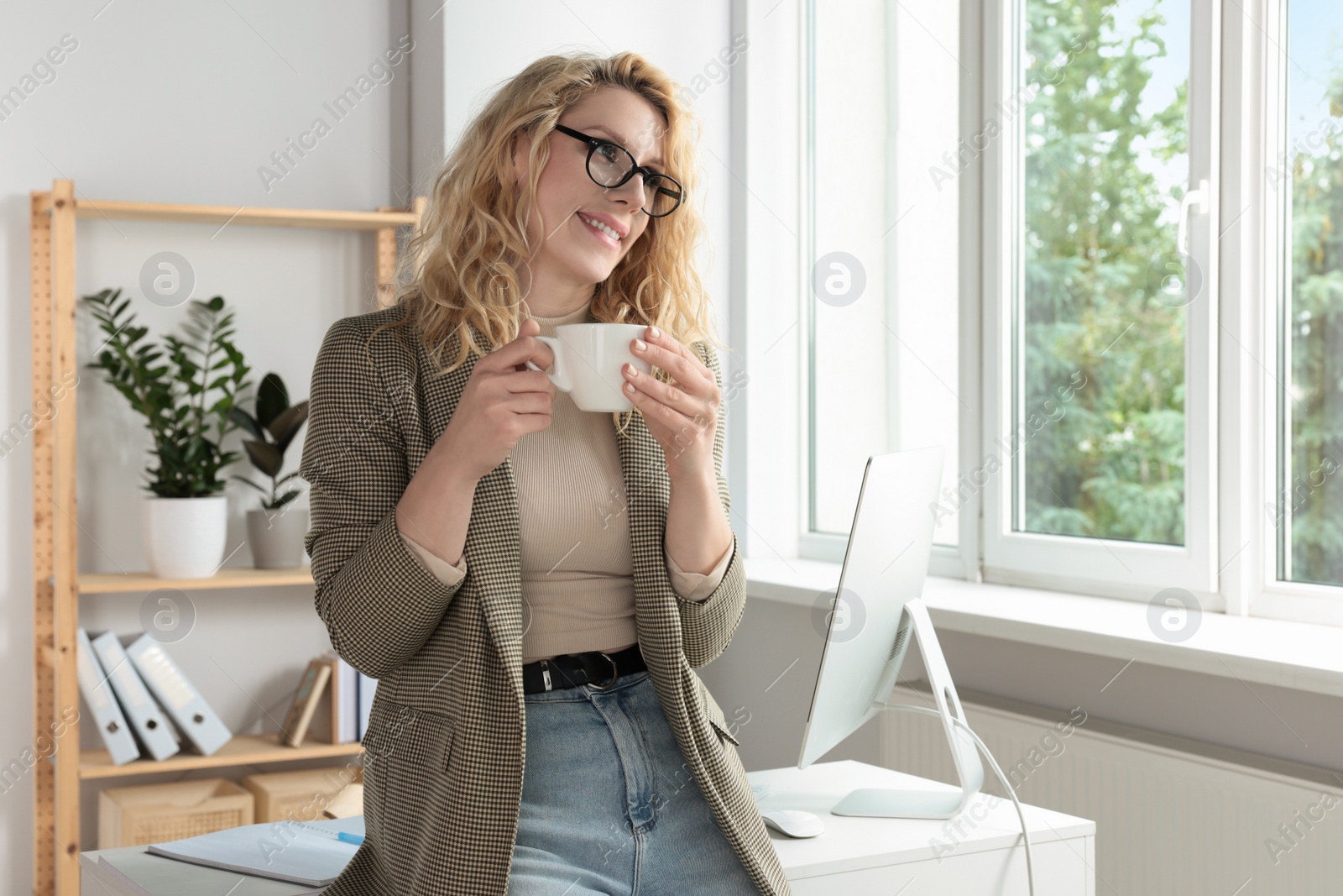 Photo of Beautiful young woman with cup of coffee near window in office