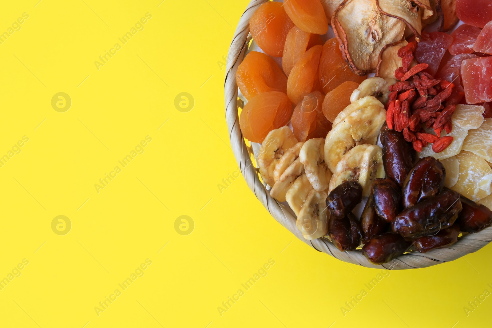 Photo of Wicker basket with different dried fruits on yellow background, top view. Space for text