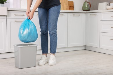 Photo of Woman taking garbage bag out of trash bin in kitchen, closeup