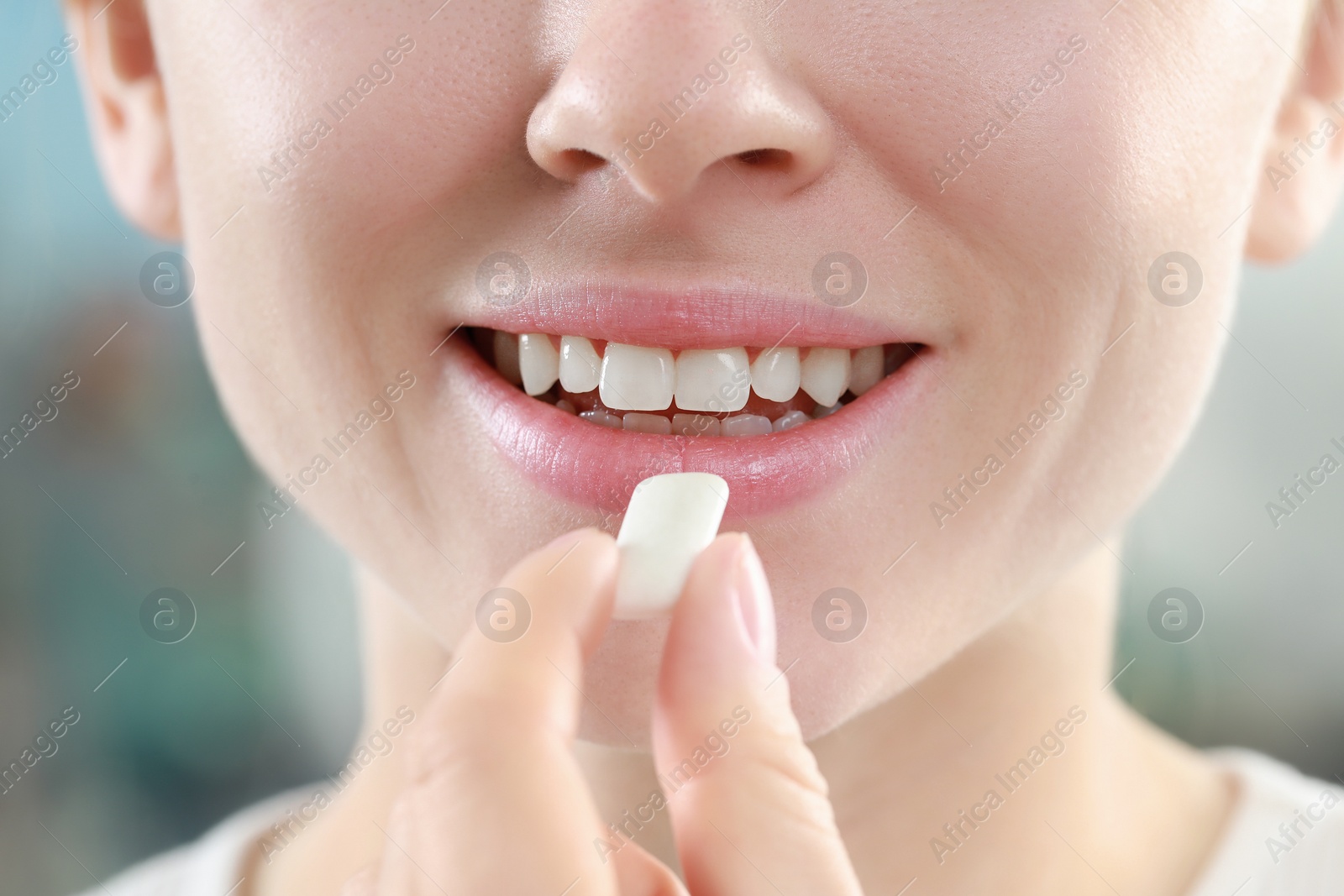 Photo of Woman putting chewing gum piece into mouth on blurred background, closeup