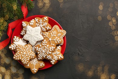 Photo of Tasty Christmas cookies with icing, fir tree branches and ribbon on black table, flat lay. Space for text