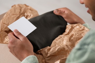 Young man holding greeting card near parcel with Christmas gift, closeup