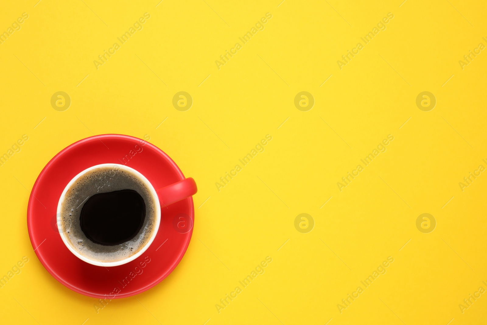 Photo of Aromatic coffee in red cup on yellow background, top view. Space for text