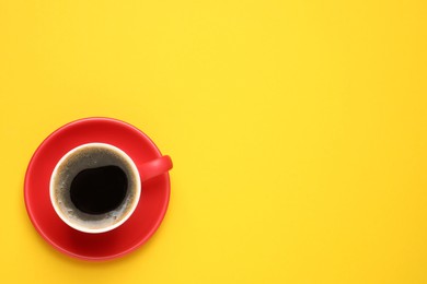 Photo of Aromatic coffee in red cup on yellow background, top view. Space for text