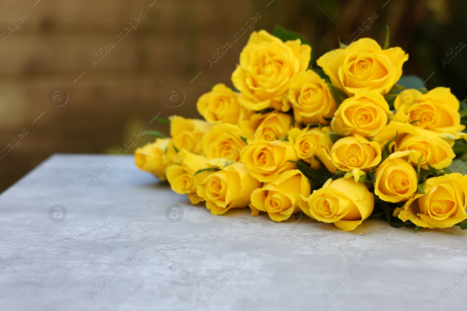 Photo of Beautiful bouquet of yellow roses on light table outdoors, space for text