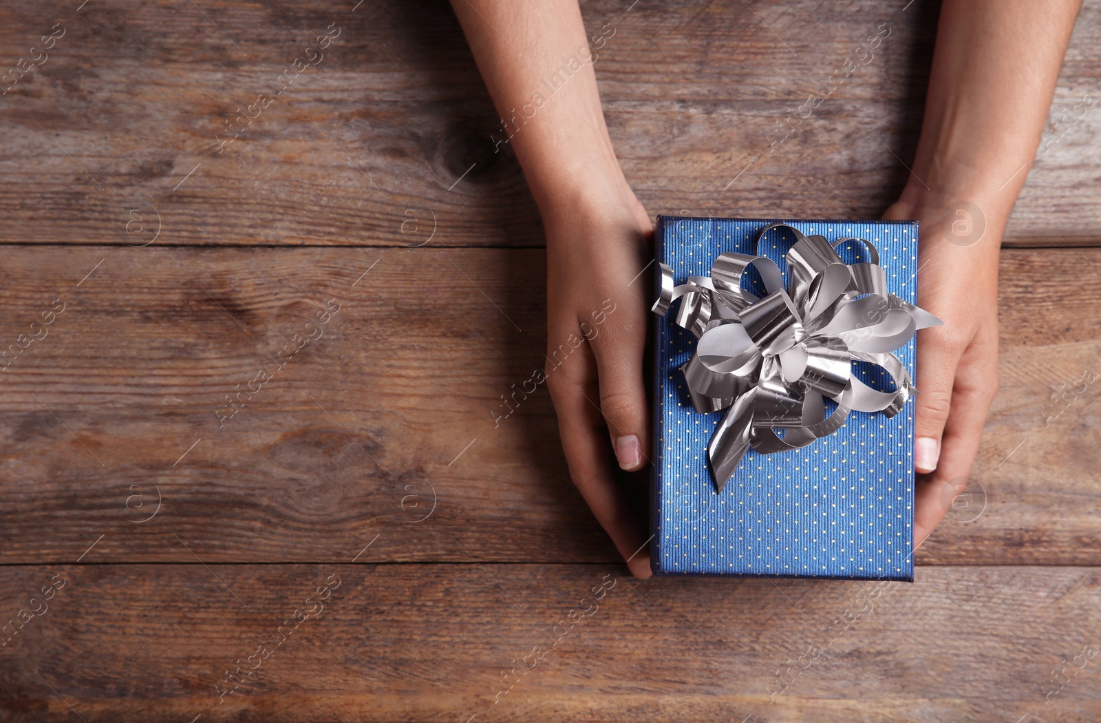 Photo of Woman holding beautiful gift box over wooden table, top view. Space for text