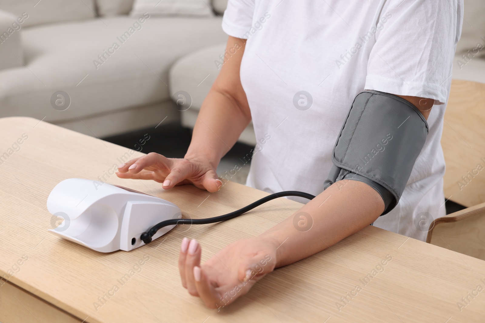 Photo of Woman measuring blood pressure at wooden table in room, closeup