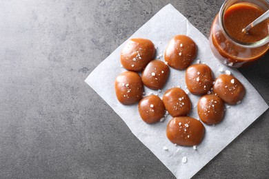 Photo of Tasty candies, caramel sauce and salt on grey table, top view. Space for text