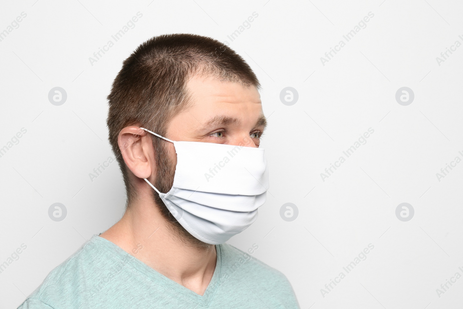 Photo of Man wearing handmade cloth mask on white background, space for text. Personal protective equipment during COVID-19 pandemic